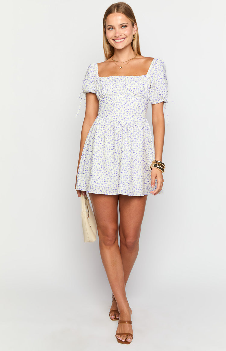 Front view of a white mini dress with purple floral print, square neckline, puff sleeves with tie details, and a shirred waist