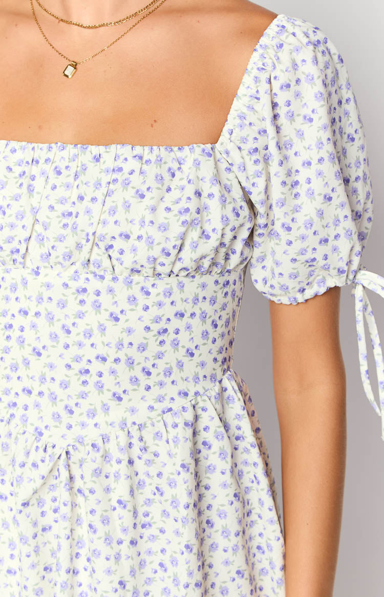 Close-up of the square neckline, gathered bust, and puff sleeve with tie detail on a purple floral mini dress
