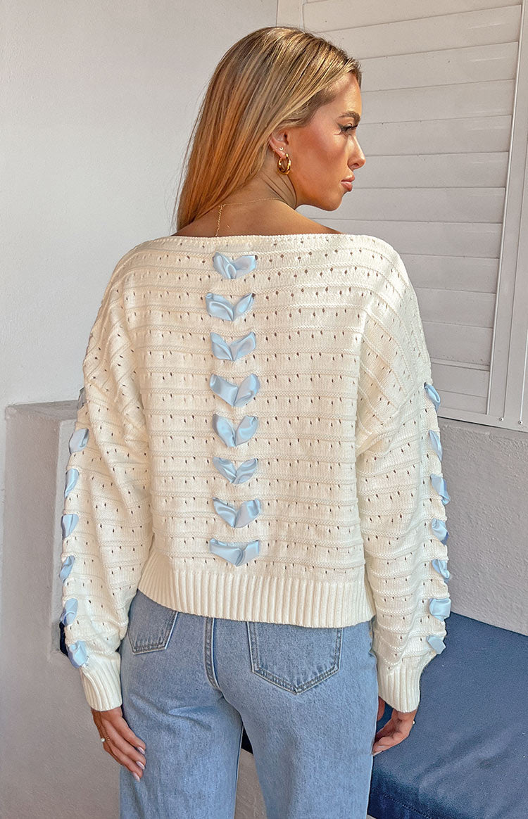 Close-up of the cream knit sweater sleeve with blue satin ribbons tied along the arm, eyelet pattern, and ribbed cuff