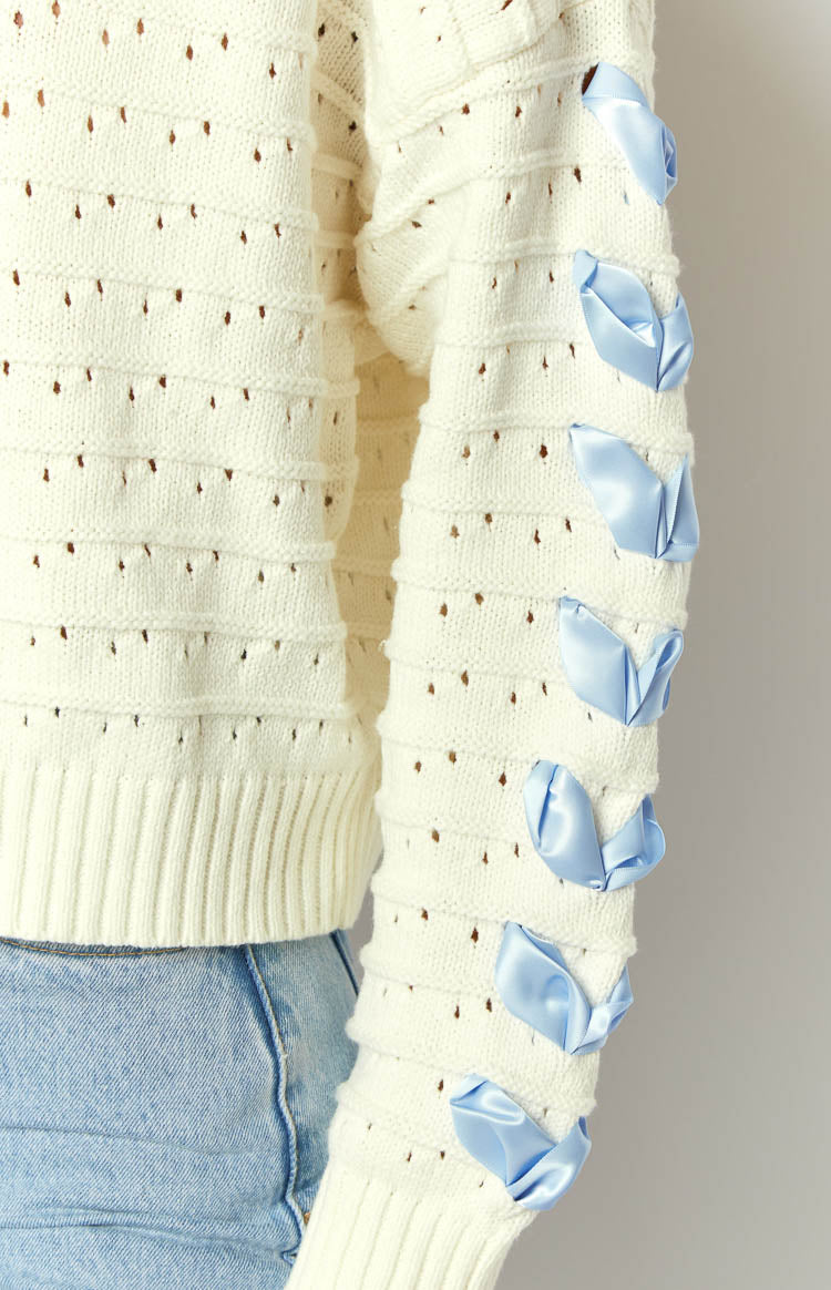 Rear view of the white knit sweater with a boat neck and light blue satin ribbon details on the back and sleeves