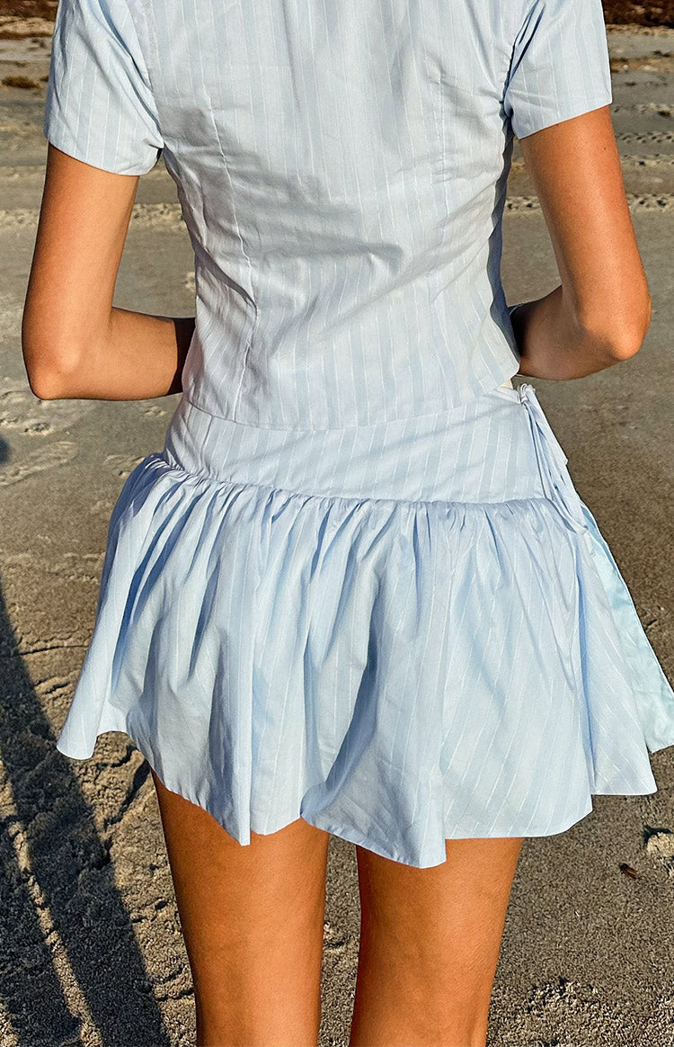 Rear view of a light blue pinstripe mini skirt with a gathered hem and side tie waist detail