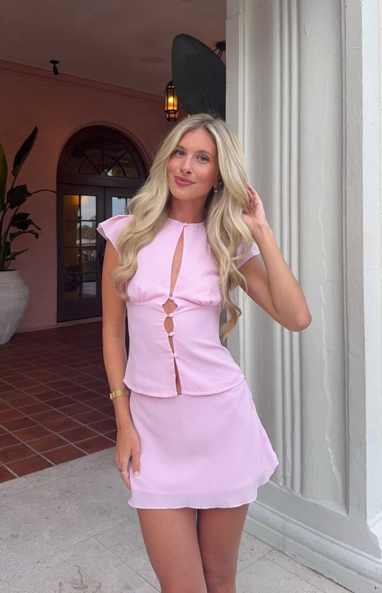 Pink woven top with a round neck keyhole, button-front cutouts, and short flutter cap sleeves