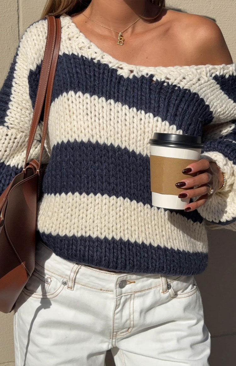 Off-the-shoulder neckline of a navy and cream striped chunky knit sweater with a relaxed fit