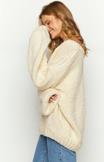 Side view of an oversized cream chunky knit sweater with voluminous long sleeves and an off-shoulder neckline