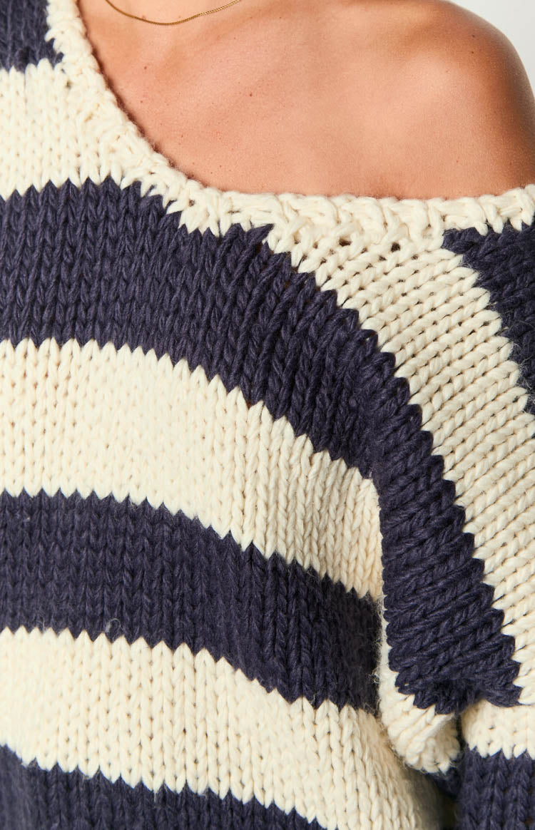 Close-up of the chunky knit texture and navy and cream stripes of the off-shoulder sweater neckline