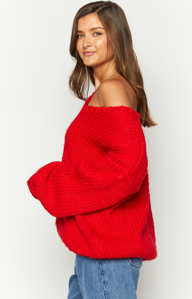 Side view of a red chunky knit sweater with an off-shoulder neckline and wide voluminous sleeves