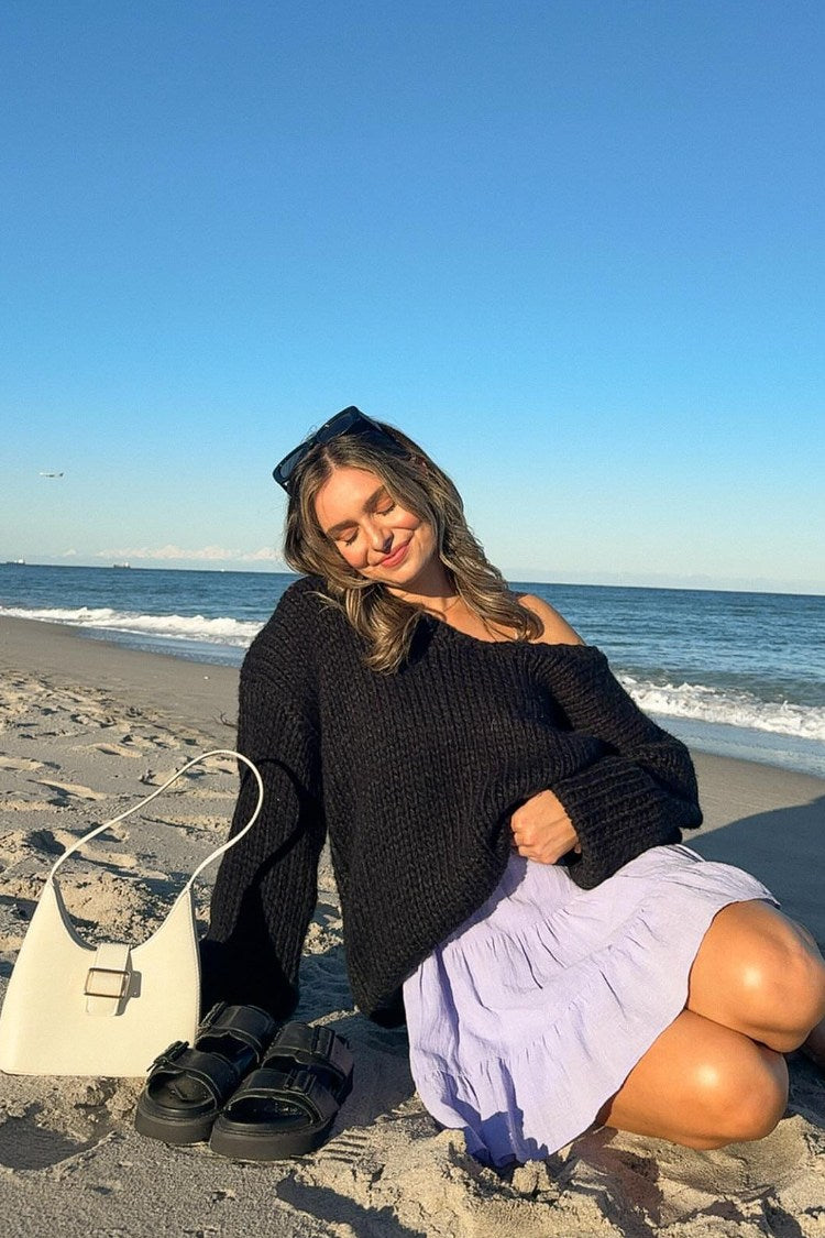 Black chunky knit sweater worn off one shoulder, showing the wide neckline and ribbed texture
