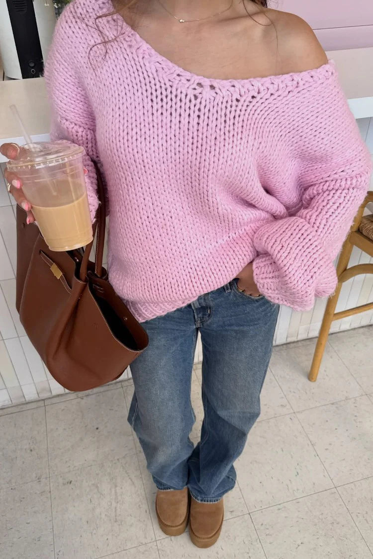Rear view of a light pink chunky knit sweater worn off-shoulder with wide long sleeves and a relaxed fit