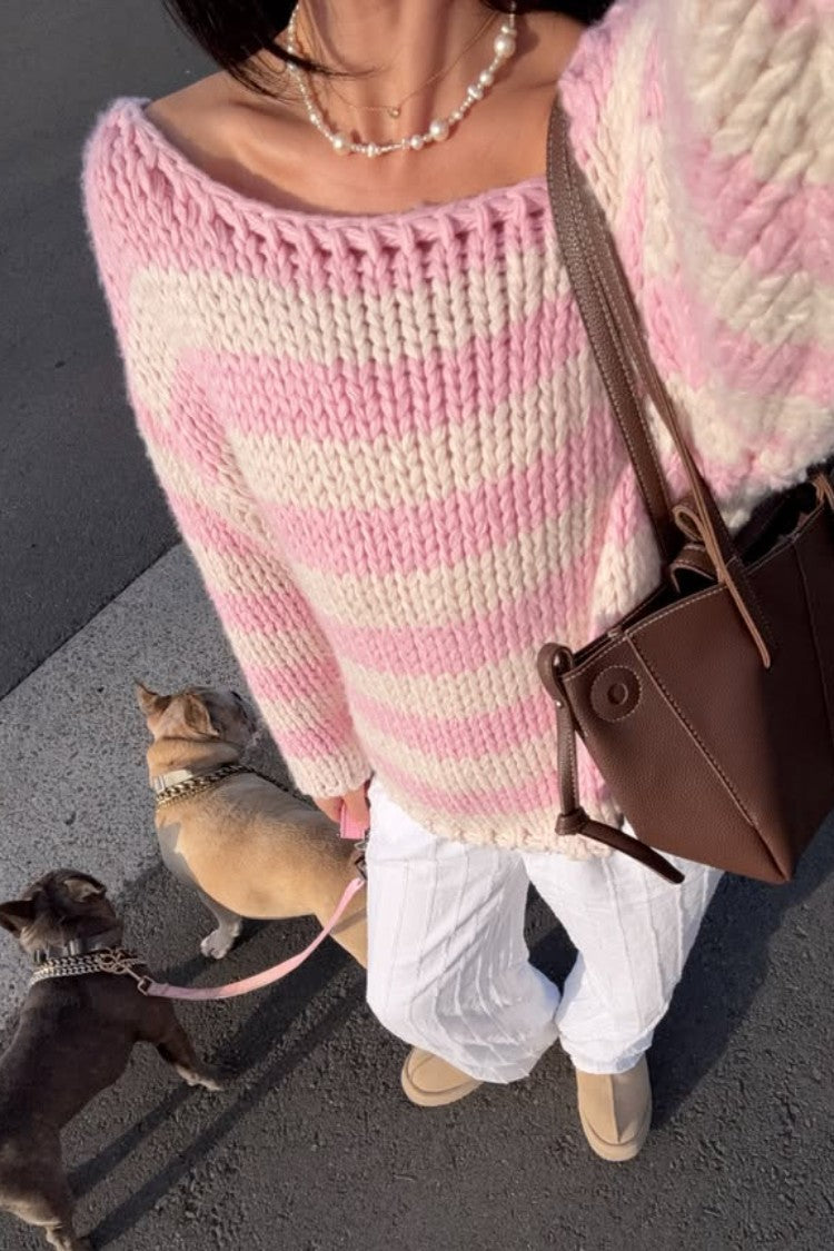 Close-up of a pink and white striped chunky knit sweater with a wide boat neckline and distressed hem