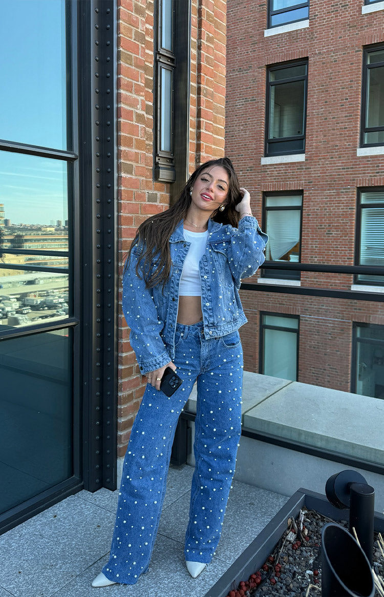 Side view of mid wash denim high waisted jeans with scattered pearl embellishments and raw hem