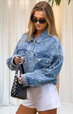 Front view of an oversized mid-wash denim jacket with all-over pearl embellishments and button-front
