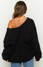 Black chunky knit sweater worn off one shoulder, showing the wide neckline and ribbed texture