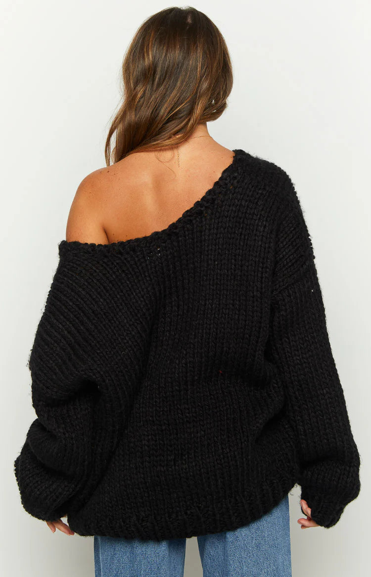 Black chunky knit sweater worn off one shoulder, showing the wide neckline and ribbed texture