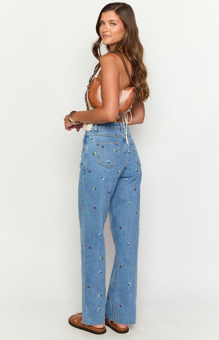 Rear view of light blue straight leg jeans with all-over colourful floral embroidery, back pockets, and raw uneven hem