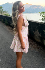 Side view of a pink floral mini dress with tie-shoulder straps, deep armholes, and a ruched waist leading to a flowy tiered s