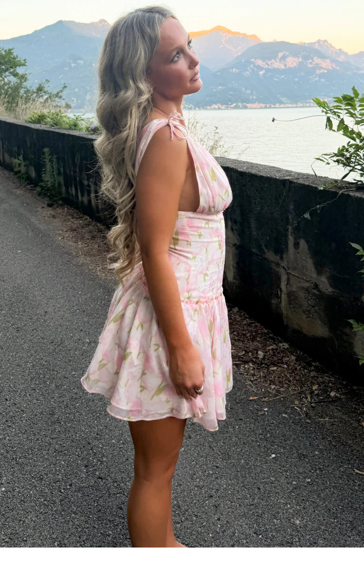 Side view of a pink floral mini dress with tie-shoulder straps, deep armholes, and a ruched waist leading to a flowy tiered s
