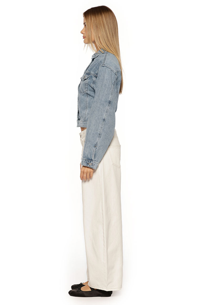 Side view of a mid wash denim jacket showing the cropped length and long sleeves with buttoned cuffs