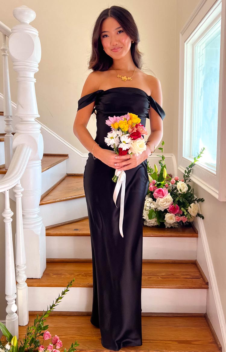 Full length view of a black off-shoulder maxi dress with a draped neckline and flowing skirt