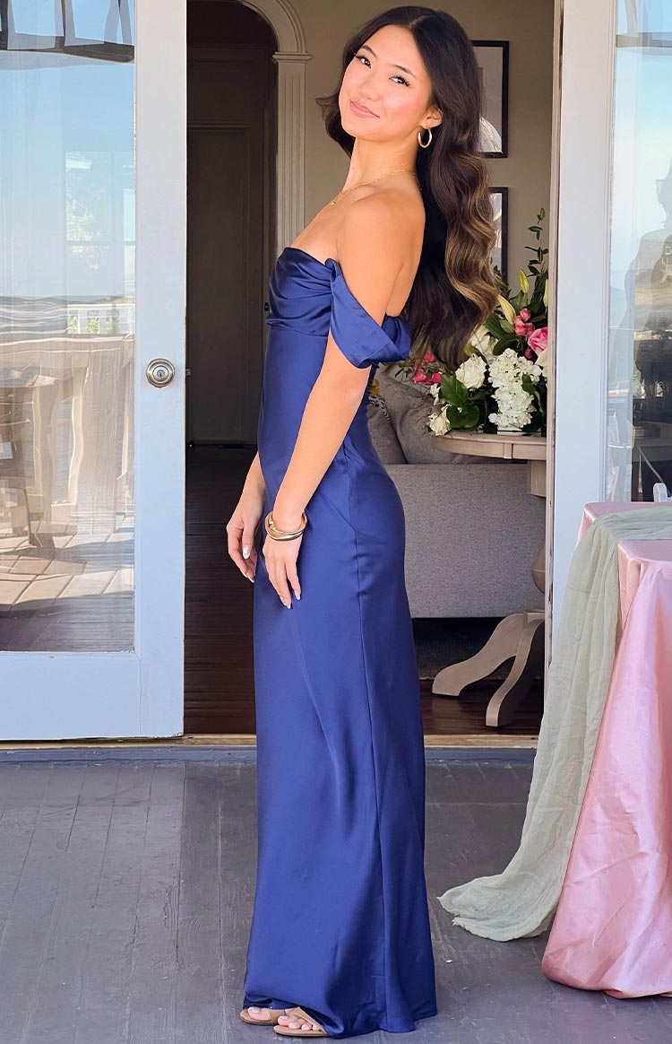 Side view of a navy off-shoulder maxi dress with draped sleeves and a fitted silhouette