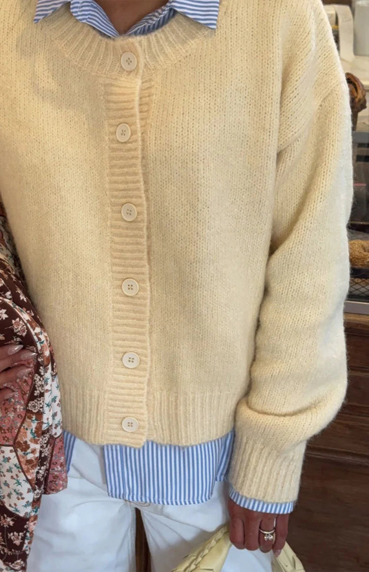 Close-up of a butter yellow knit cardigan worn open, showing the ribbed cuffs and matching buttons