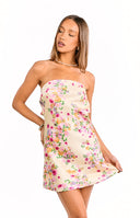 Back view of our model wearing a pale yellow mini dress with a multicolored floral pattern. The dress features a large cut-out at the back with a tie closure at the top.