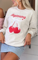 Close-up of the oat marle crew neck sweater showing the red 'Beginning' text and cherry graphic with white bow