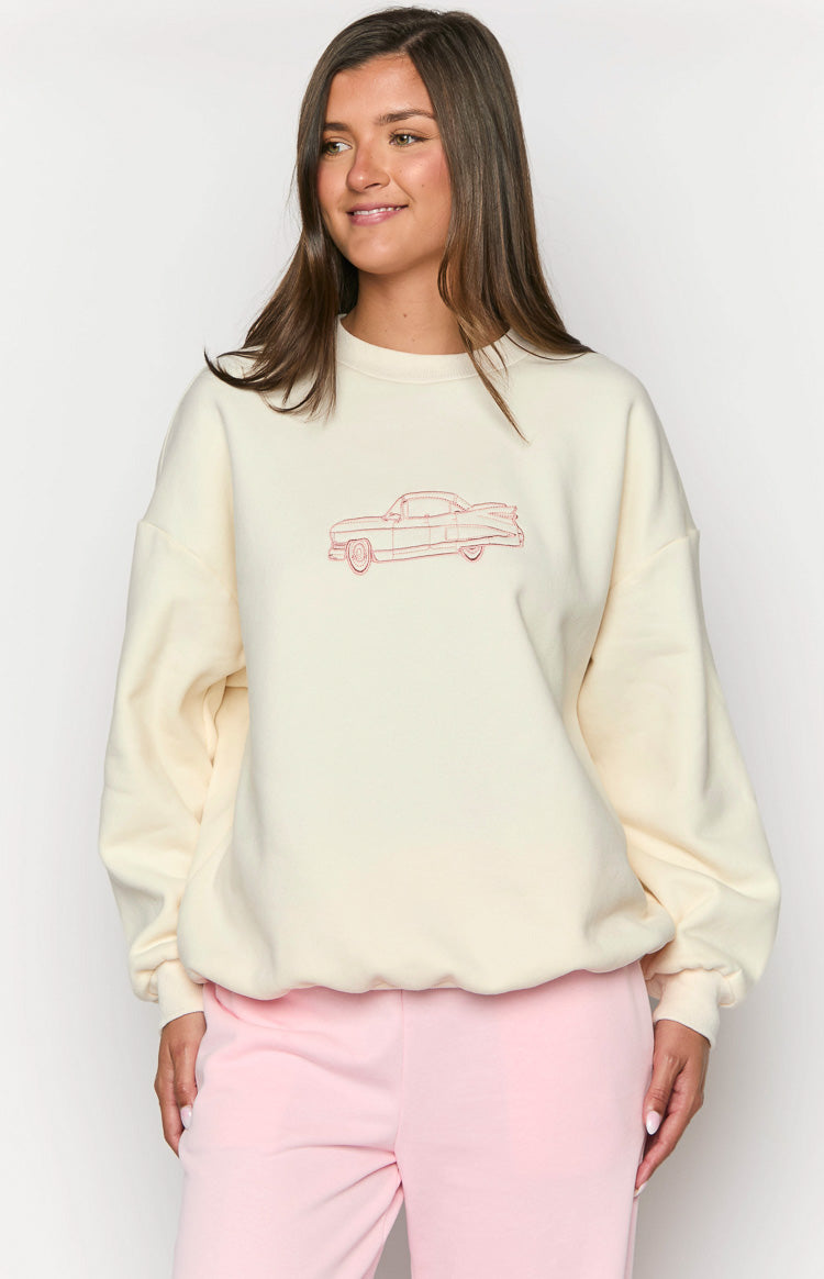 Close-up of the red embroidered vintage car graphic on the front of a cream crew neck sweater