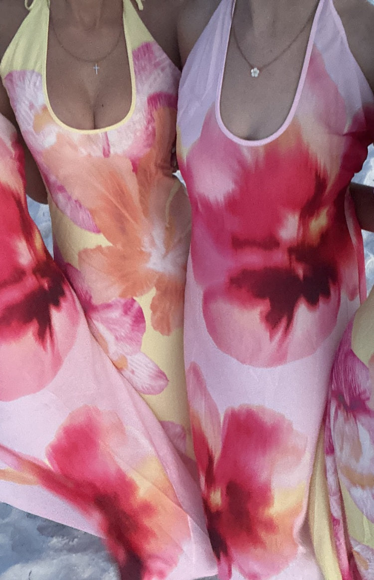 Close-up of two halter maxi dresses with scoop necklines, showing vibrant pink and orange floral prints on yellow and light p