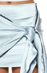 Close-up of the knotted front detail on a light blue satin mini skirt with dark blue lace edges