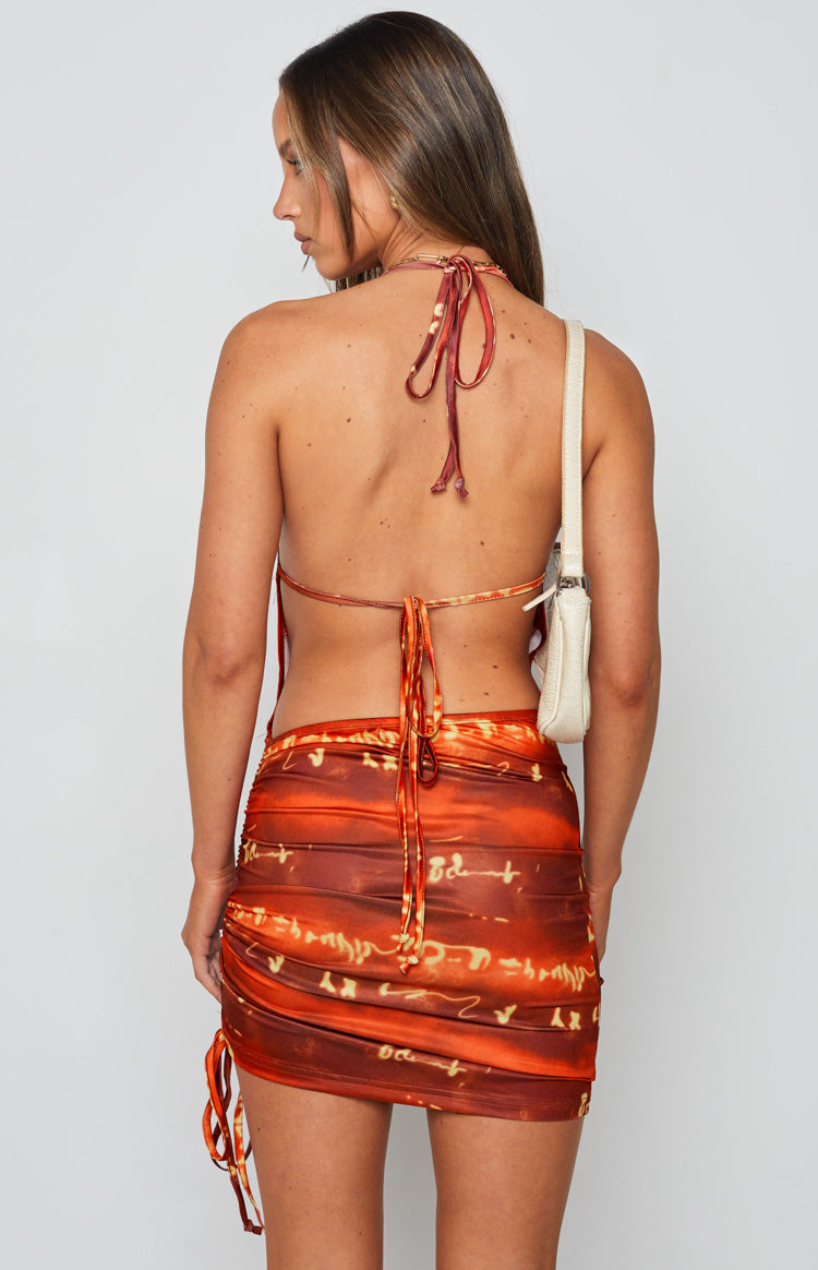 Rear view of the red and orange patterned mini dress with a halter neck tie, open back, and ruched skirt