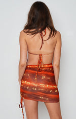 Rear view of the red and orange abstract patterned halter mini dress with an open back, tie-up halter neck, and adjustable waist ties