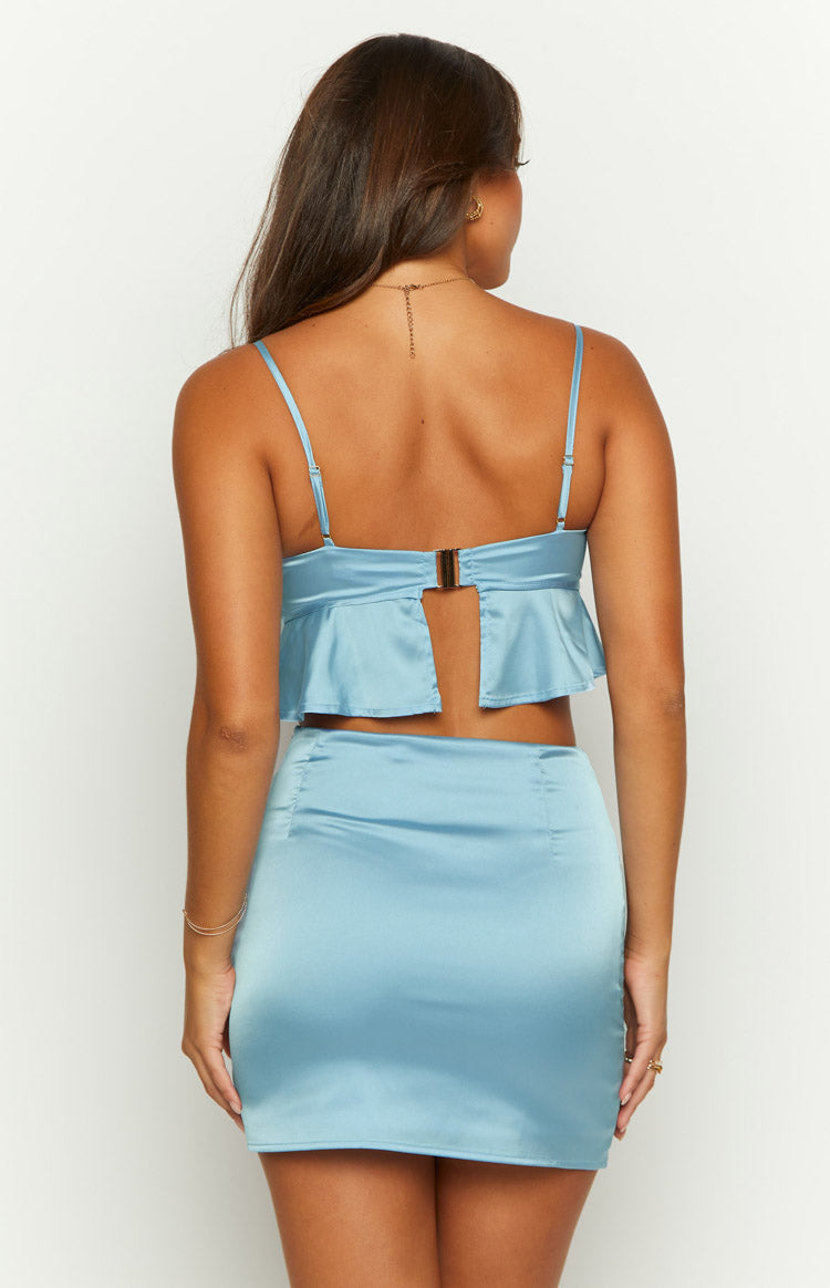 Rear view of a blue satin crop top with open back, gold clasp, ruffled hem, adjustable straps, and matching mini skirt