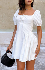 Front view of a white mini dress showing the fitted bodice, tie-front square neckline, and gathered asymmetric skirt