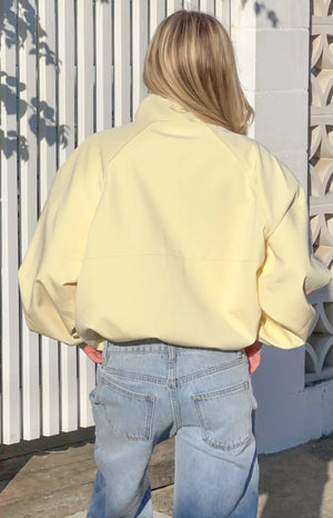 Rear view of a yellow funnel neck sports jacket with raglan sleeves and an elasticated hem