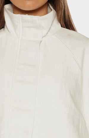 Close-up of the cream funnel neck sports jacket showing the crinkled fabric texture and raglan sleeve seam