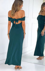 Rear view of a teal crepe off the shoulder maxi dress with a large bow tie and ruched detail on the lower back
