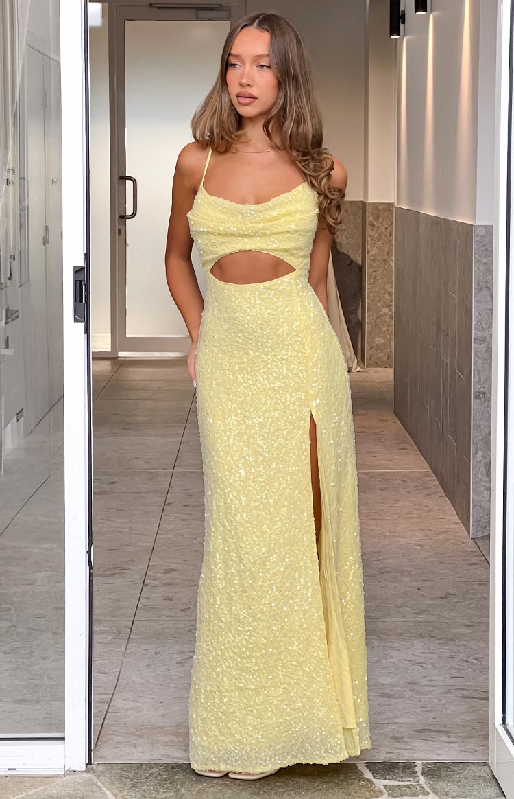 Full length view of a yellow sequin maxi dress with spaghetti straps, a cowl neckline, waist cut-out, and high leg split