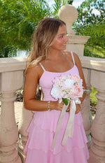 Side view of a pink maxi dress with pearl shoulder straps, a low scoop back, and tiered ruffle skirt