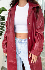 Close-up of the red PU trench coat showing the shiny fabric, silver buttons, and adjustable cuff straps