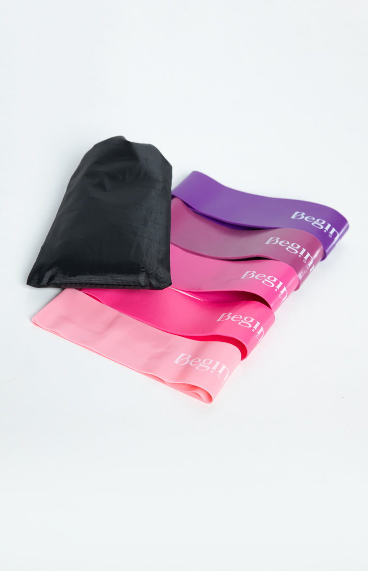 Five resistance bands in shades of pink and purple fanned out, with a black drawstring storage pouch