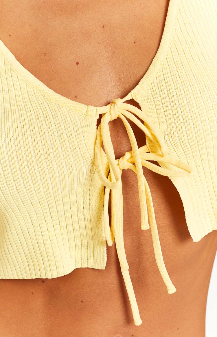 Close-up of the yellow ribbed knit crop top's front tie closure, knotted at the chest with long ties