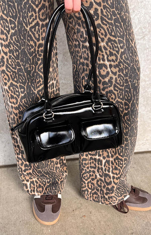 model holding a black leather handbag wearing leopard print pants and brown sneakers