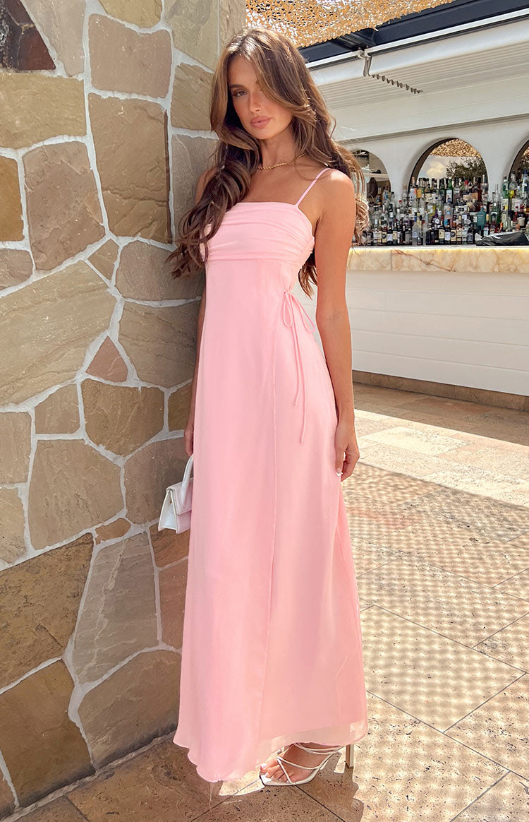 Full length view of a pink maxi dress with a ruched bust, thin spaghetti straps, and side tie details