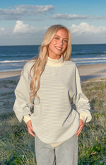Front view of a blue and cream horizontal stripe mock neck sweater with oversized fit and cream ribbed cuffs