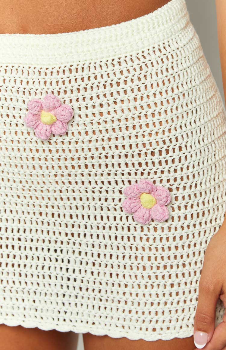 Close-up of the open-knit white crochet mini skirt texture with two pink and yellow flower appliques