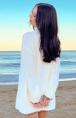 Rear view of a cream knit sweater dress with black contrast trim on the cuffs and hem
