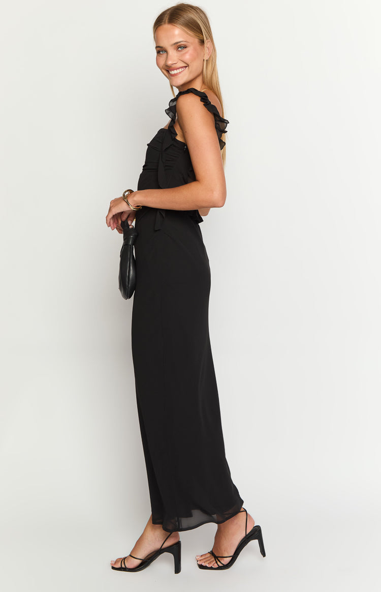 Side view of a black maxi dress with ruffled shoulder straps, a ruched bodice, and a flowy skirt with a sheer hem