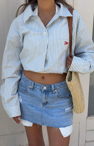 Close-up of the light wash denim low rise mini skirt featuring distressed details and a raw frayed hem with white lining