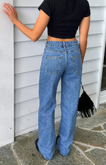 Rear view of mid-wash denim jeans with eyelet trim along the top of the back pockets and a straight leg fit