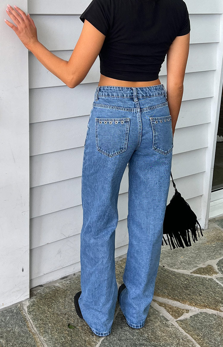 Rear view of mid-wash denim jeans with eyelet trim along the top of the back pockets and a straight leg fit